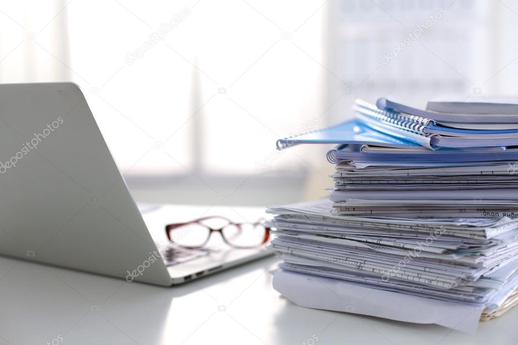 Laptop with stack of folders on table on white background