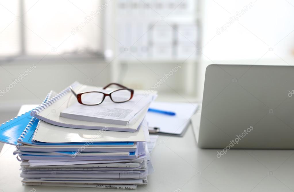 Laptop with stack of folders on table on white background