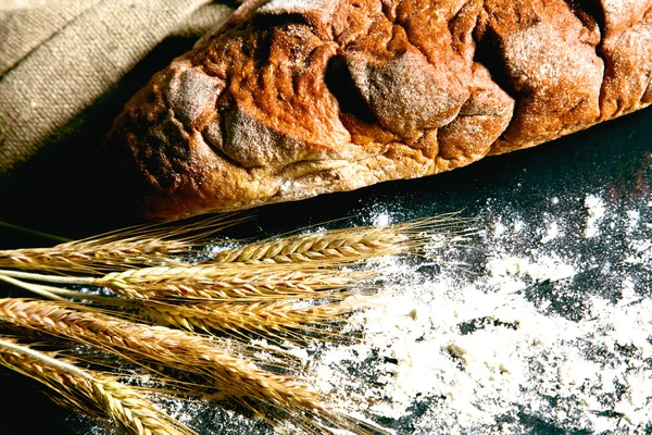 Pan crujiente rústico y espigas de trigo en una mesa de madera oscura — Foto de Stock