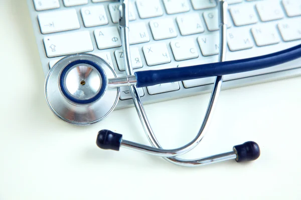 Medicinska stetoskop nära en laptop på bord, på vitt — Stockfoto