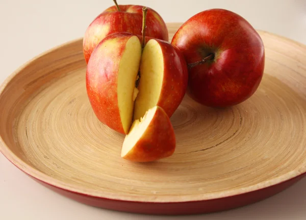 Tre mele rosse si trovano su un piatto di legno — Foto Stock