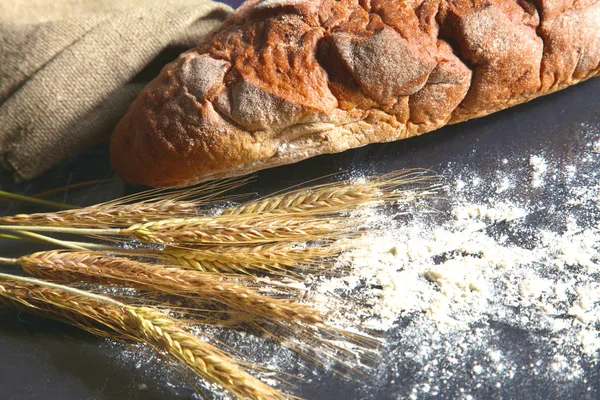 Rustieke knapperig brood en tarwe oren op een donkere houten tafel — Stockfoto