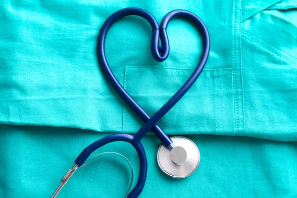 Estetoscopio que forma el corazón y el portapapeles en uniforme médico, primer plano — Foto de Stock