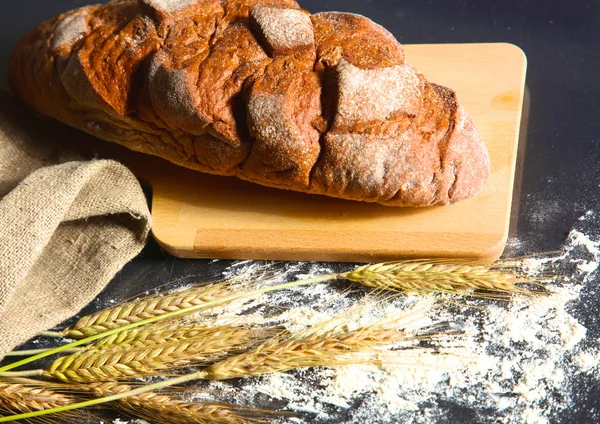 Pan crujiente rústico y espigas de trigo en una mesa de madera oscura — Foto de Stock
