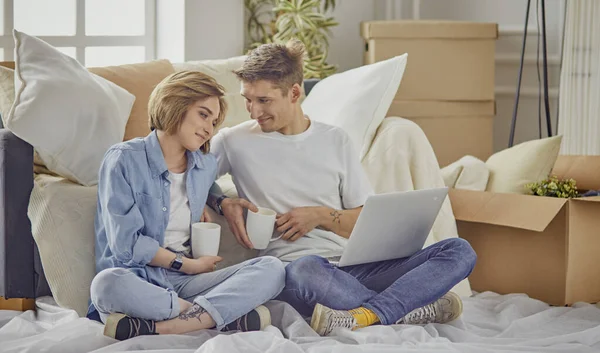 Retrato de pareja feliz mirando el ordenador portátil juntos sentados en una casa nueva, rodeados de cajas — Foto de Stock