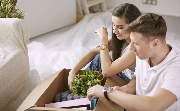 Retrato de casal feliz olhando para o computador portátil juntos sentados em casa nova, cercados de caixas — Fotografia de Stock