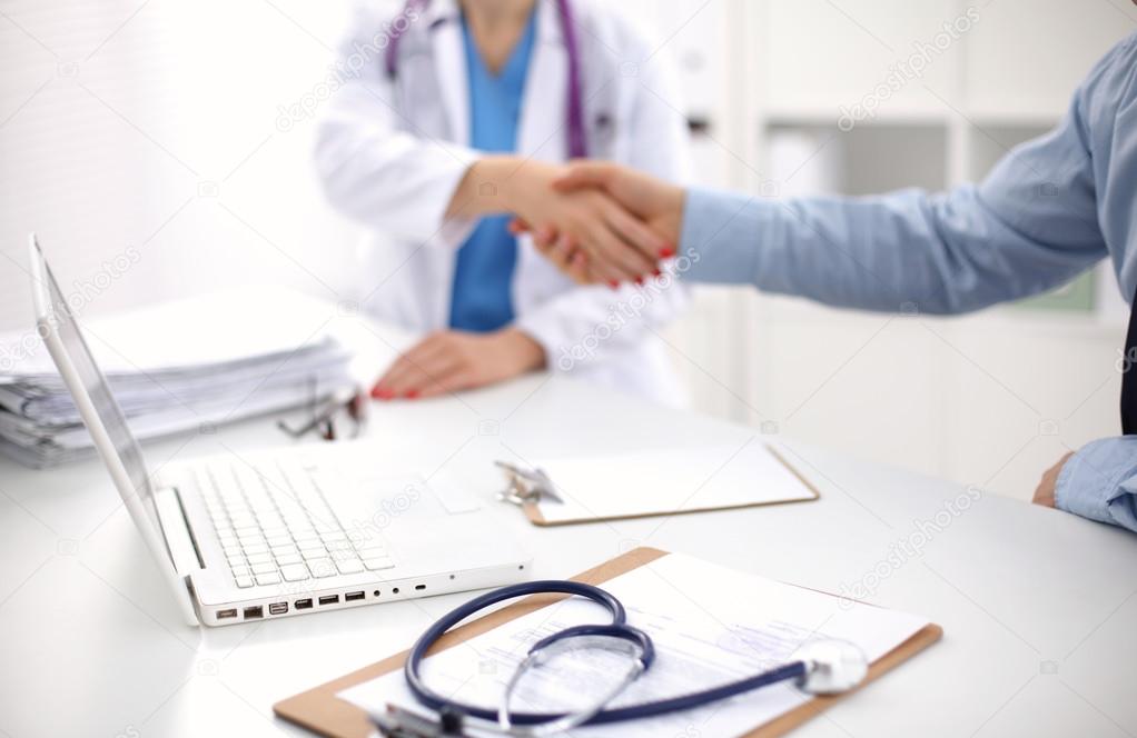 Attractive female doctor shaking a patients hands in her office