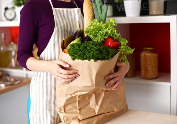 Assorted fruits and vegetables in brown grocery bag holding a young girl