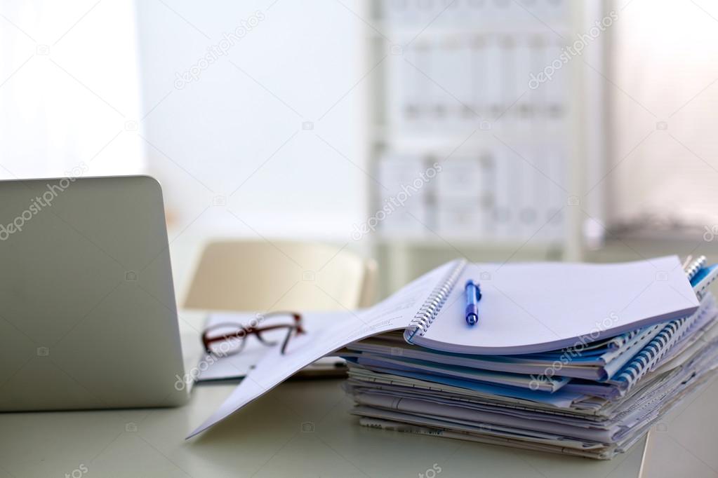 a stack of papers on the desk with a computer