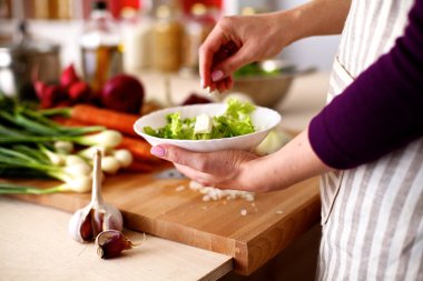 Mutfakta sebze doğrayan genç bir kadın.