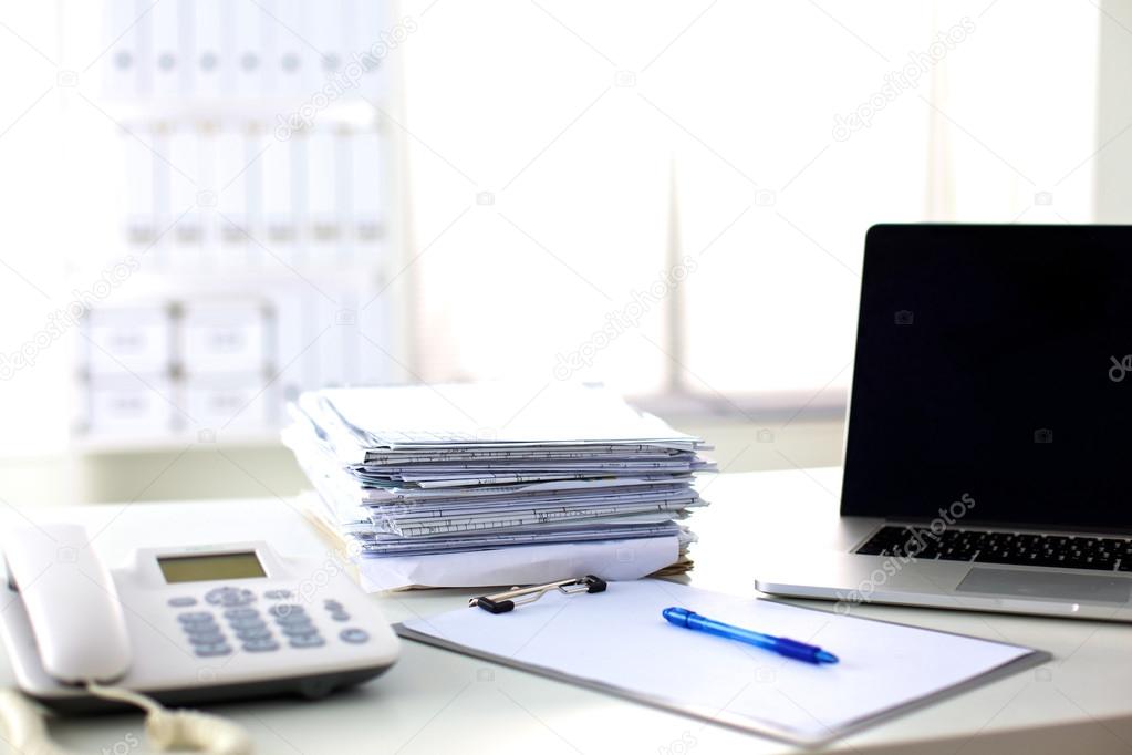 Laptop with stack of folders on table on white background