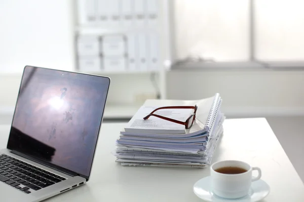Laptop with stack of folders on table on white background — Stock Photo, Image