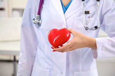 Genç kadın doktor ofisinde kırmızı bir kalp tutan