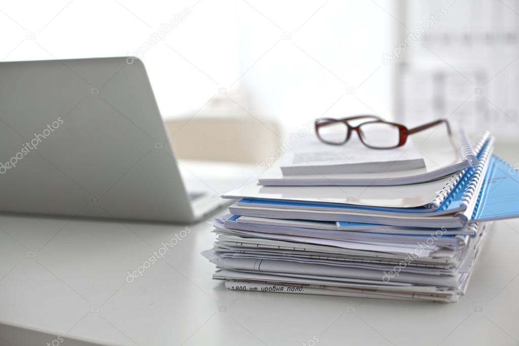 Laptop with stack of folders on table on white background