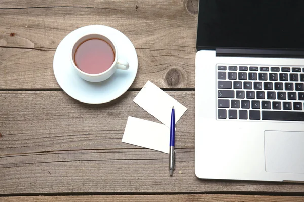 Blank business cards with pen, laptop and tea cup on wooden office table