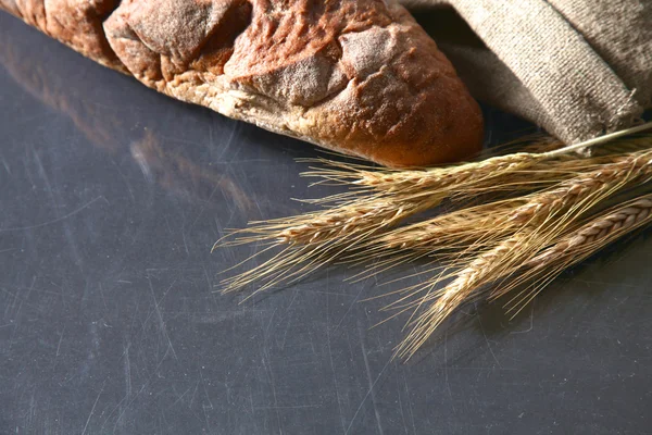 Rustieke knapperig brood en tarwe oren op een donkere houten tafel — Stockfoto