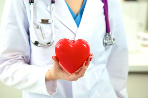 Médico con estetoscopio examinando el corazón rojo — Foto de Stock