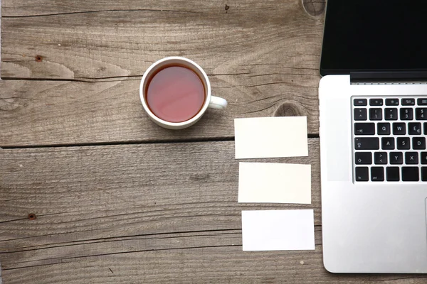 Cartões de visita em branco com caneta, laptop e xícara de chá na mesa de escritório de madeira — Fotografia de Stock