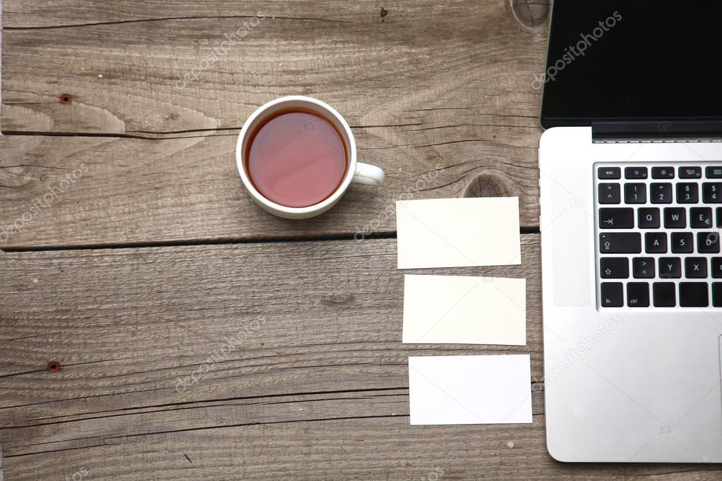 Blank business cards with pen, laptop and tea cup on wooden office table