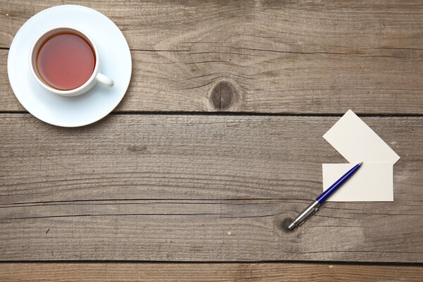 Пустые визитки с ручкой и чайной чашкой на деревянном столе офиса
