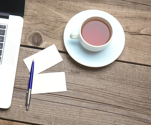 Tarjetas de visita en blanco con bolígrafo, portátil y taza de té en la mesa de madera —  Fotos de Stock