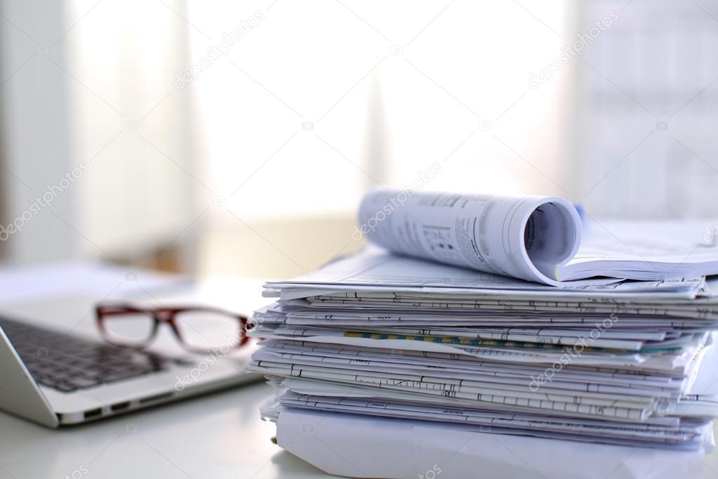 Laptop with stack of folders on table on white background