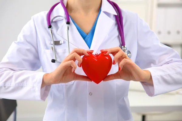 Genç kadın doktor ofisinde kırmızı bir kalp tutan — Stok fotoğraf