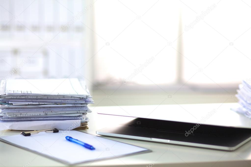 Laptop with stack of folders on table on white background