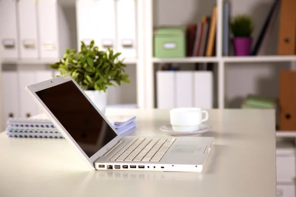 Close up view of a work desk interior with a laptop computer, a cup of coffee and white curtains on a sunny day Royalty Free Stock Photos