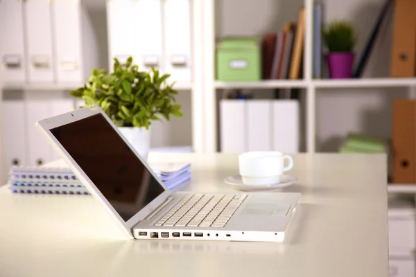 Close up view of a work desk interior with a laptop computer, a cup of coffee and white curtains on a sunny day Stock Image