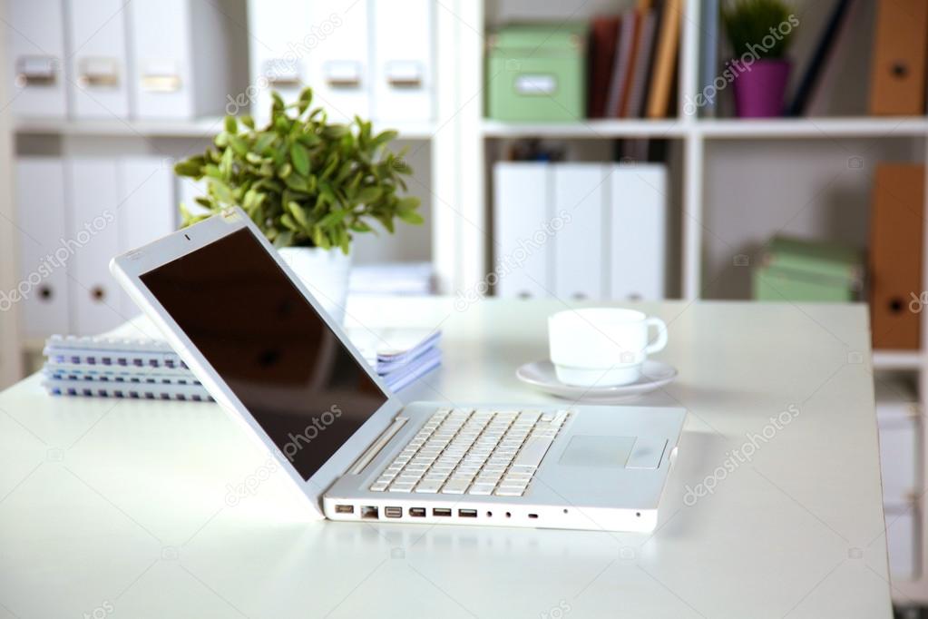 Close up view of a work desk interior with a laptop computer, a cup of coffee and white curtains on a sunny day