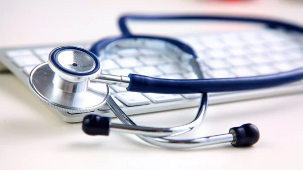 Un estetoscopio médico cerca de una computadora portátil en la mesa, en blanco — Foto de Stock