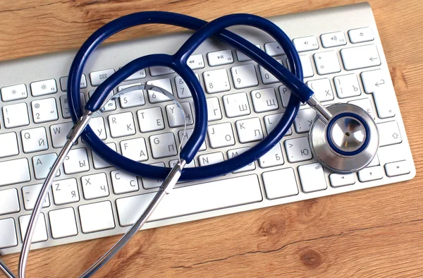 Medicinsk stetoskop nära en laptop på ett träbord, på vitt — Stockfoto