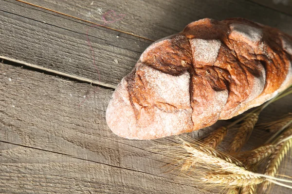 质朴的脆皮面包和小麦耳朵，黑暗的木制的桌子上 — 图库照片