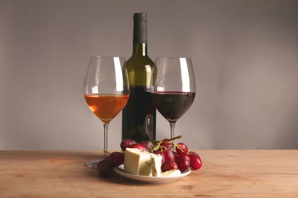 Bodegón refinado de vino, queso y uvas en bandeja de mimbre sobre mesa de madera —  Fotos de Stock