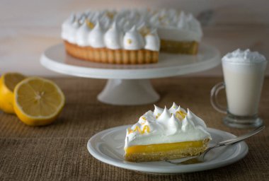 Limonlu turta sergisi vajilla blanca junto a limones y una bebida caliente ayık un mantel de tela rustica
