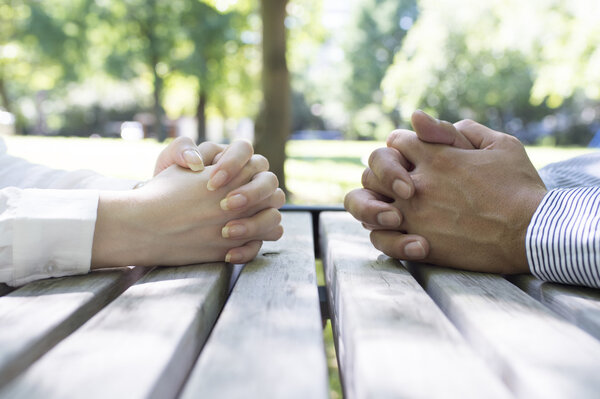 Man and woman sits at a wood desk with hands clasped