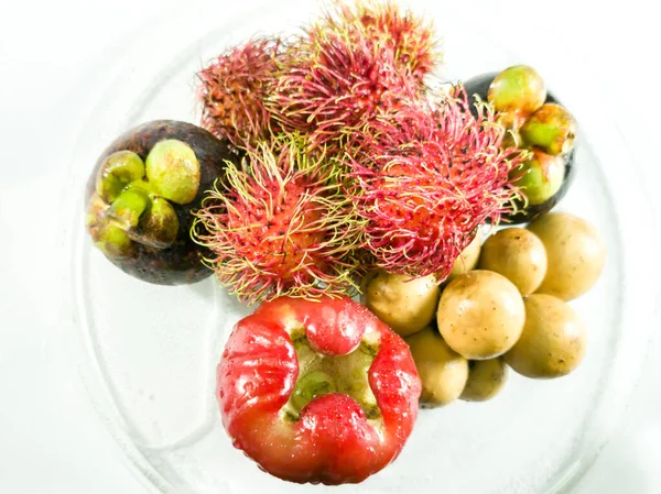 High angle. Thai fruits, rose apple, rambutan, mangosteen, Lansium demesticum, on a clear glass cup, sprinkled with water, white background.