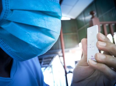 Asyalılar beyaz koruyucu maskeler takıyor. Tüm yüzü göremiyorum. Antijen test kiti, test sonuçları 1 düz çizgi sembolü gösteriyor. Yani evde enfeksiyon yok..