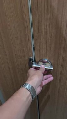 4K video kaydı. Gümüş saatli bir insan eli, kilidi açmak için ahşap kapıya modern krom mandalı çevirir.