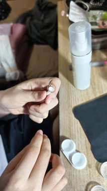 Tahta masa üzerinde mercek kılıfı ve çözelti şişesi yerleştirme ya da kaldırma için hazırlanan kahverengi süslemeli lens taşıyan bir kişi