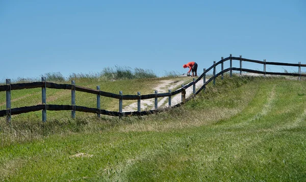 Person prepares for wind surfing on Farstad Beach , Norway. The landscape is divided by a wooden fence and make nice curve in the picture