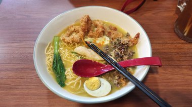 Bir kase deniz mahsulü ramen, siyah yemek çubuğu, kırmızı kaşık ve beyaz kase.