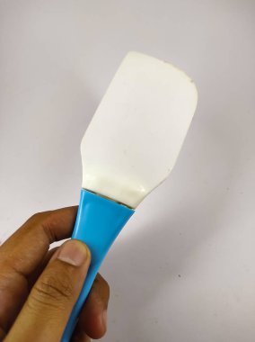 Beyaz arka planda izole edilmiş plastik bir spatula tutan sol elin fotoğrafı.