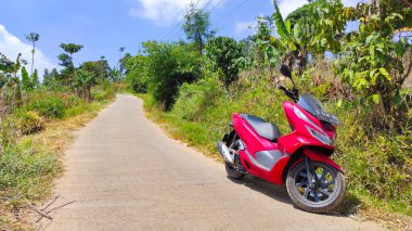 Cikancung, Batı Java, Endonezya - 26 Ağustos 2021: Yokuş aşağı giden bir yolda park etmiş kırmızı bir scooter 'ın soyut çözünmüş fotoğrafı
