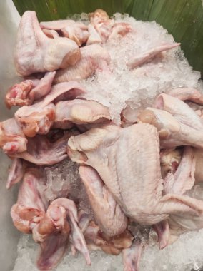 Buzdaki bir yığın tavuğun fotoğrafı. Taze kesilmiş tavuk etin tazeliğini korumak için bir dükkan vitrininde buzla sergilenir. Çiğ gıda malzemelerinin geçmişi