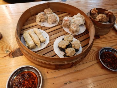 Soslu ve soğuk içeceklerle birlikte çeşitli Dim Sum tabakları içeren bir masa üstü menüsü. Tavuklu Dim sum, karides, tofu derisi ve nori bambu budan bir buharlı tencerede servis edilir. Çin mutfağı.