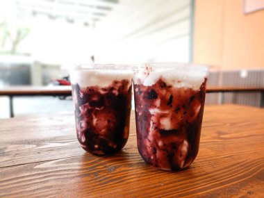 Plastik bardaklarda servis edilen yabanmersini reçelli iki süt içeceği. Ahşap bir masada iki soğuk içecek. Bokeh özgeçmişli soğuk içecekler.