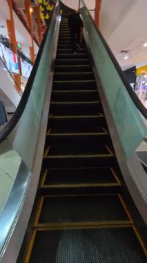 En üst kata çıkan yürüyen merdivenlerin dikey FPV klipsi. 4K HD çözünürlüklü bir alışveriş merkezindeki bir binanın katları arasındaki ulaşımın yakın çekim görüntüleri.