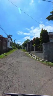 Bandung, Endonezya, 27 Ocak 2026. FPV, hasarlı ve kayalık geçiş yolları olan ıssız bir yerleşim bölgesinden geçen bir aracın dikey video klibi. POV görüntüleri 4K HD çözünürlükte.